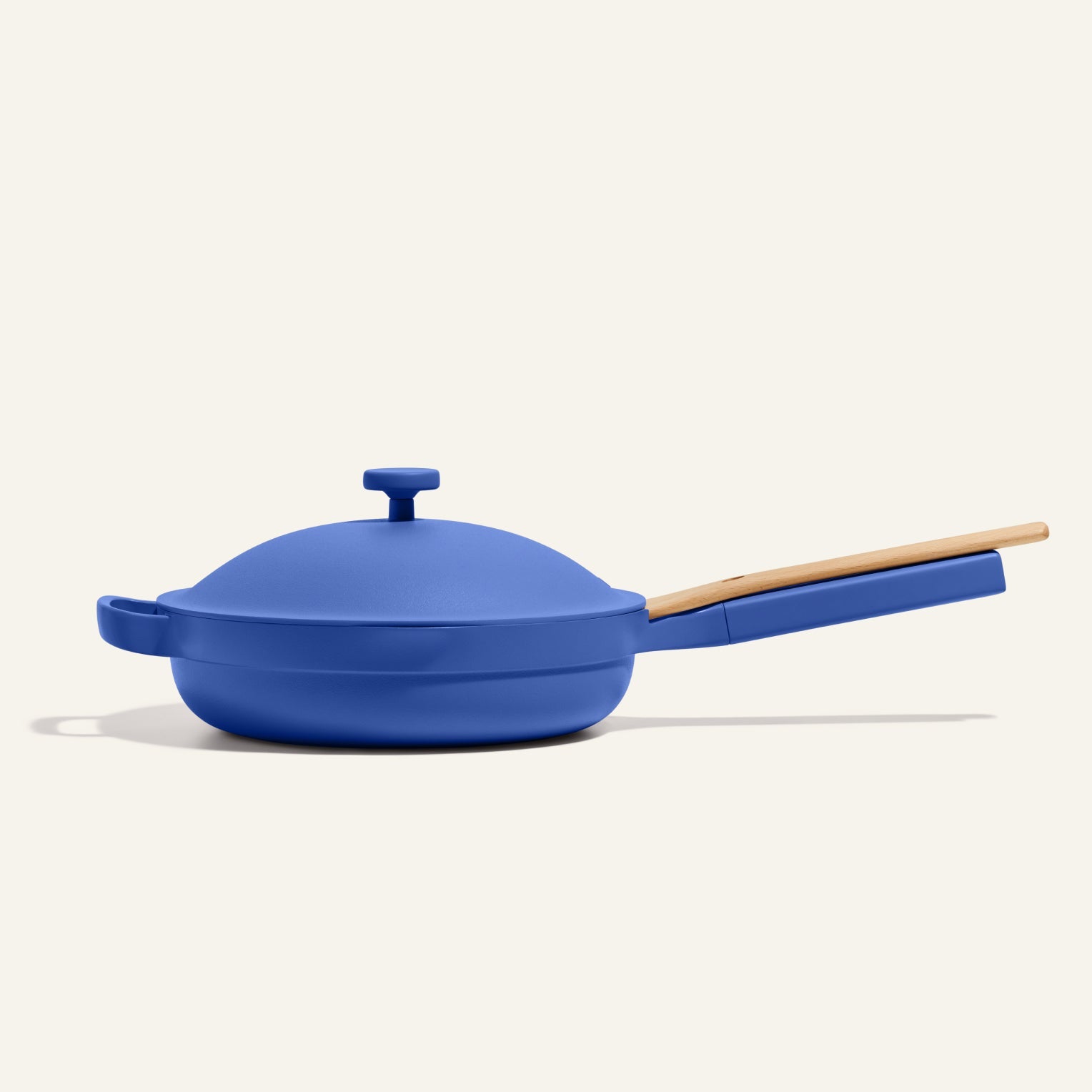 The Always Pan 2.0 is a blue nonstick frying pan with a matching lid and long wooden handle, featured against a plain light background.