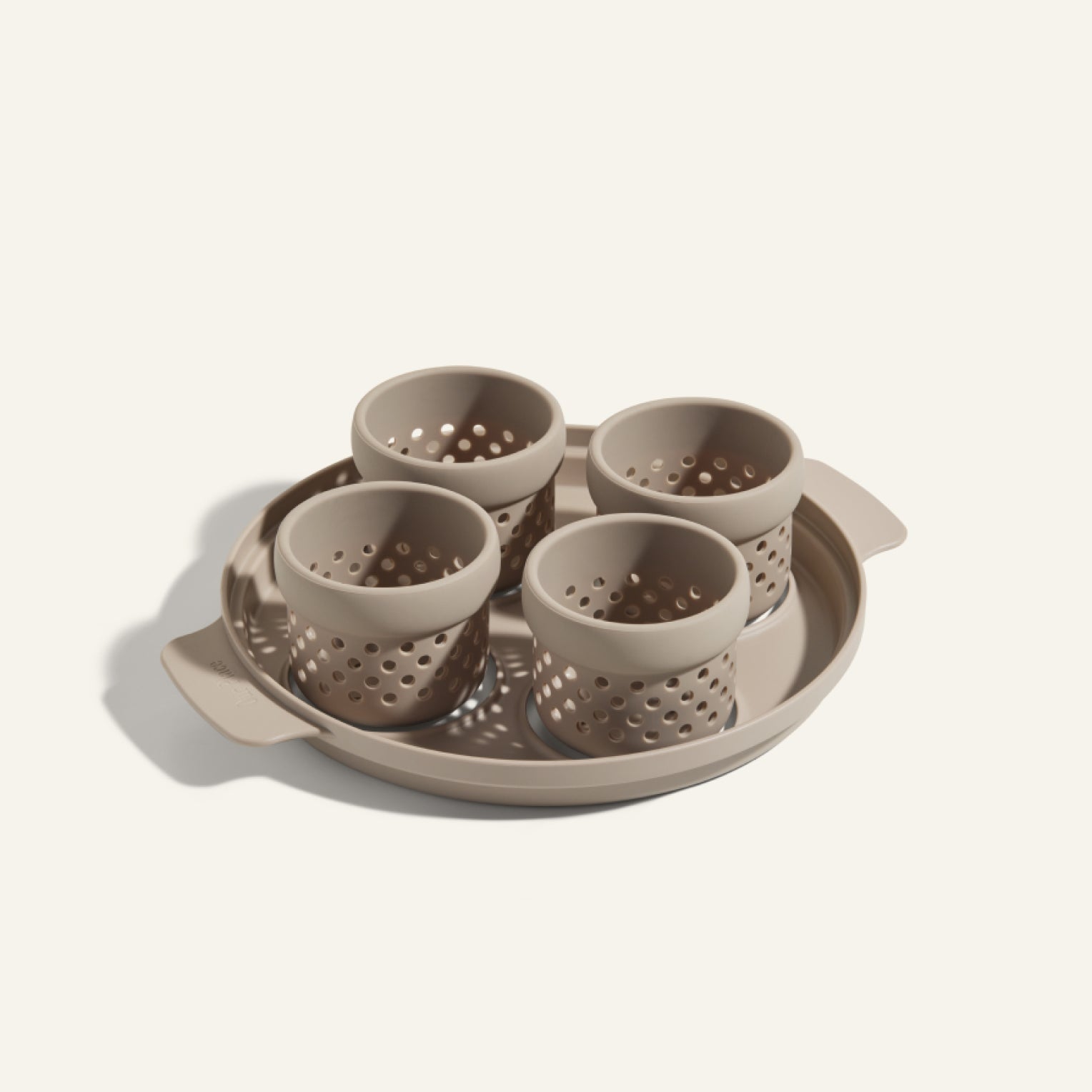 The Egg Poacher includes a beige tray and four matching perforated silicone cups, ideal for poaching eggs, all crafted from the same material and displayed against a light background.