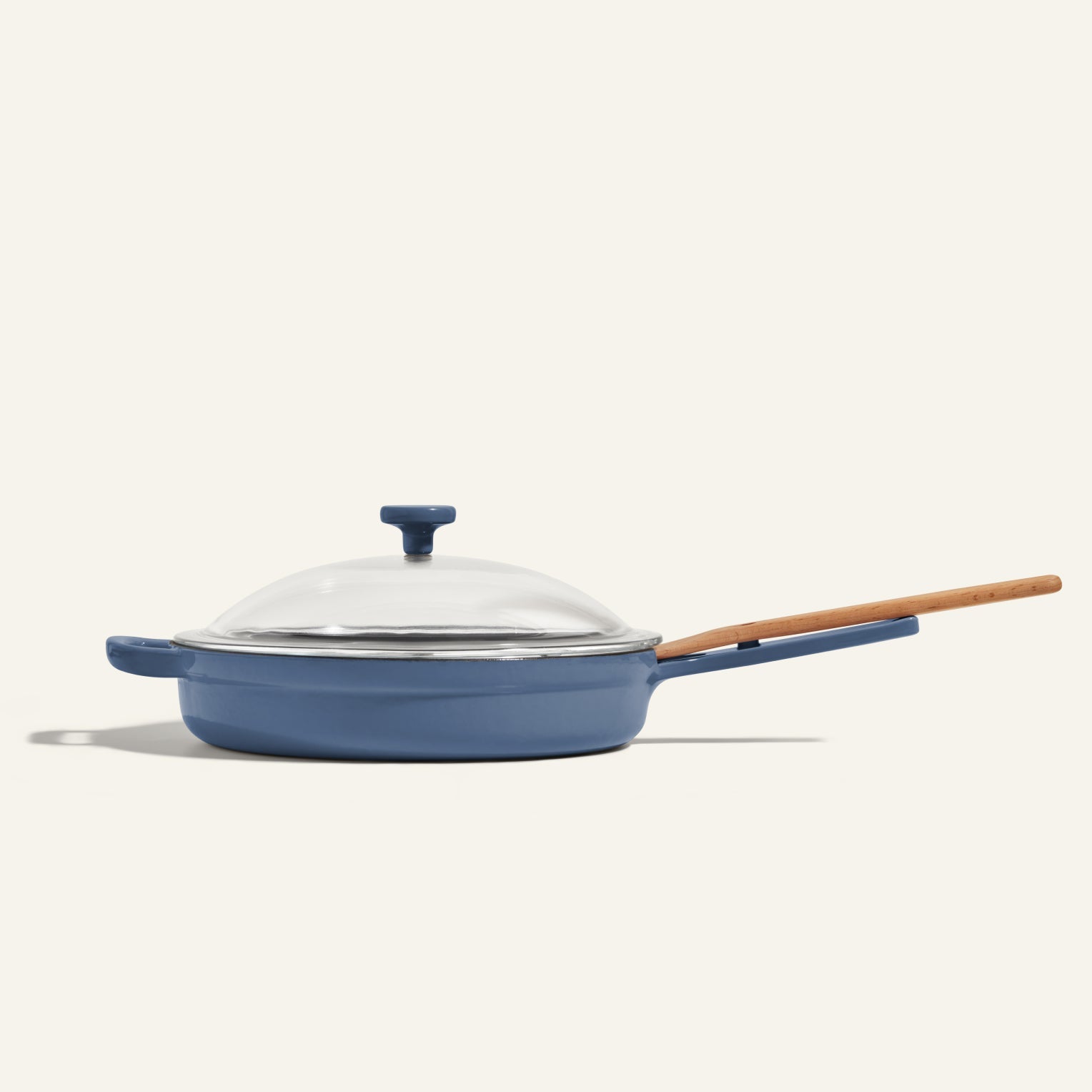 The Cast Iron Always Pan, a blue nonstick skillet with 8-in-1 versatility, includes a glass lid and wooden handle, displayed against a plain light background.