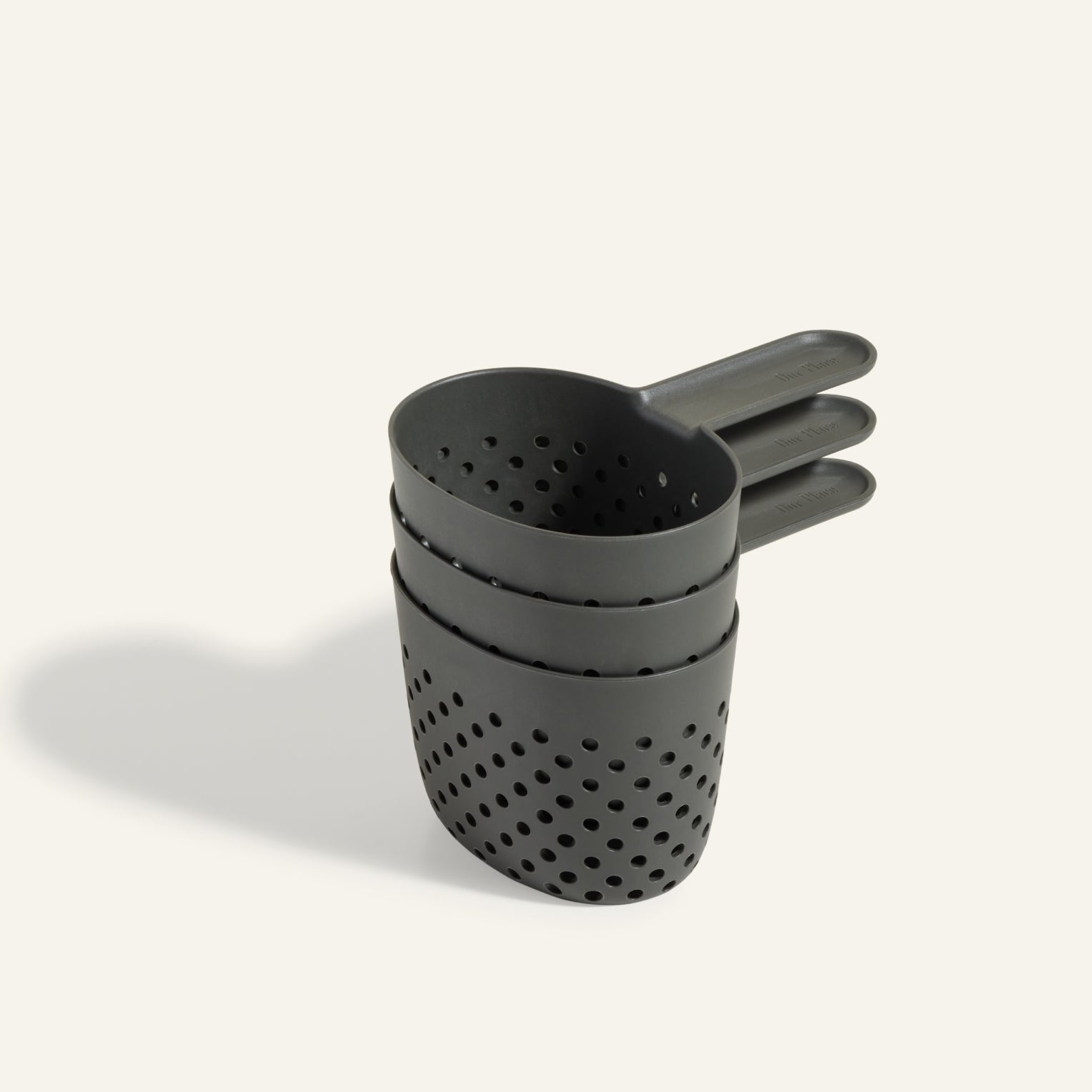Cooker Cups: a set of three black, stackable plastic measuring cups with holes—ideal for cooking multiple dishes at once and a perfect match for the Perfect Pot. Shown neatly stacked on a light background.
