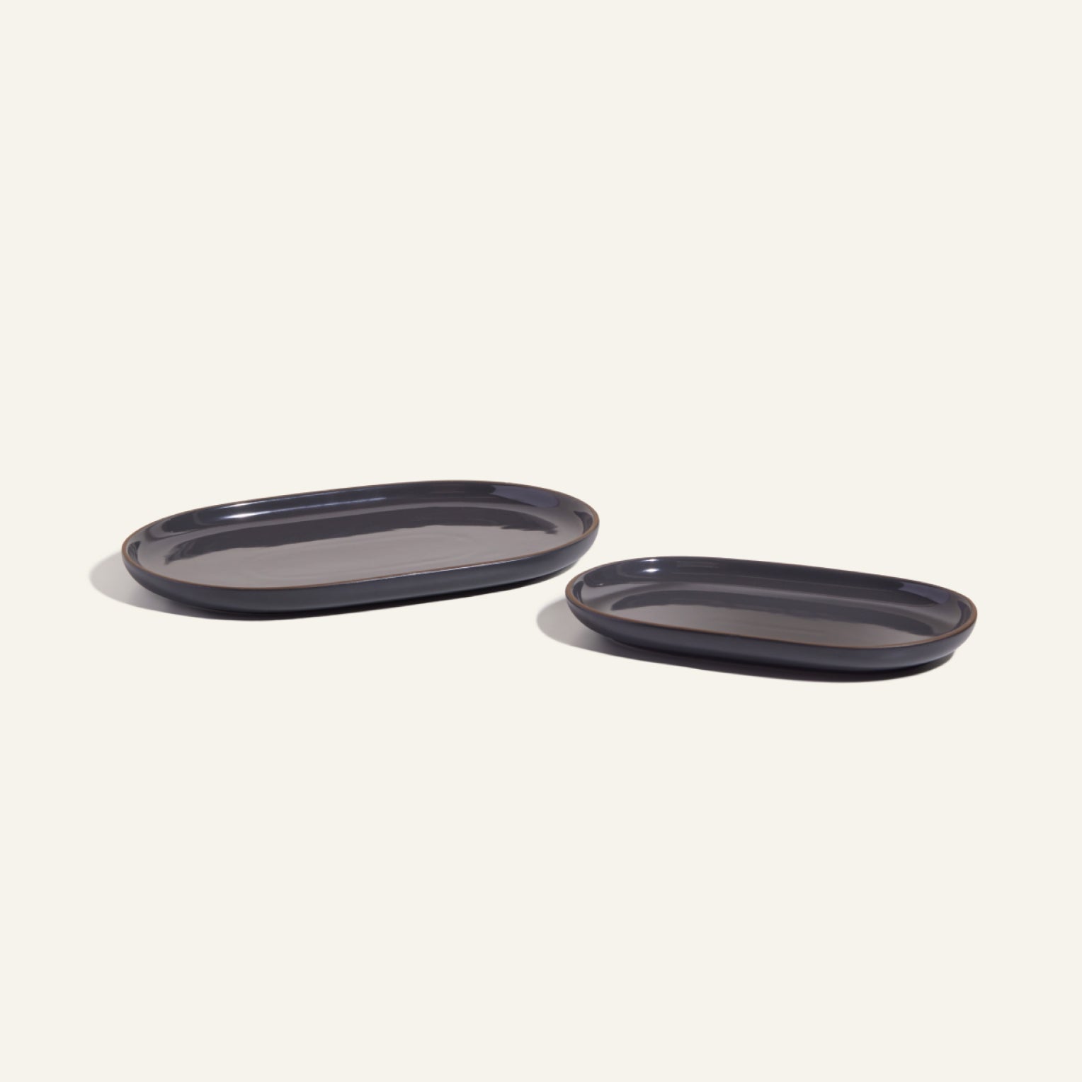 Two dark oval Serving Platters, one large and one small, arranged side by side on a light background. Their curved design makes them ideal as stackable tableware, adding elegance and versatility to your dining setup.