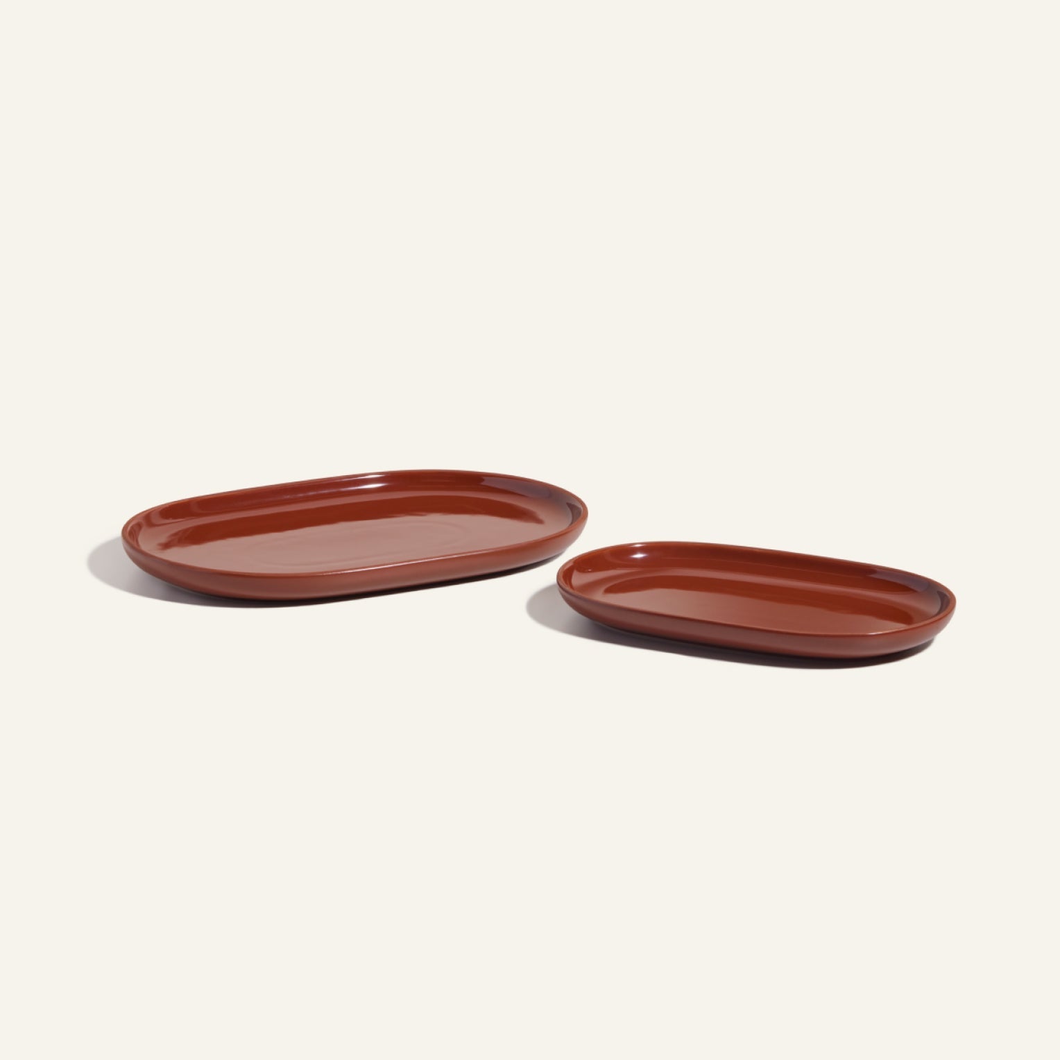 Two oval-shaped brown Serving Platters of different sizes rest on a plain background, showcasing elegant curved platters ideal for stylish, stackable tableware collections.