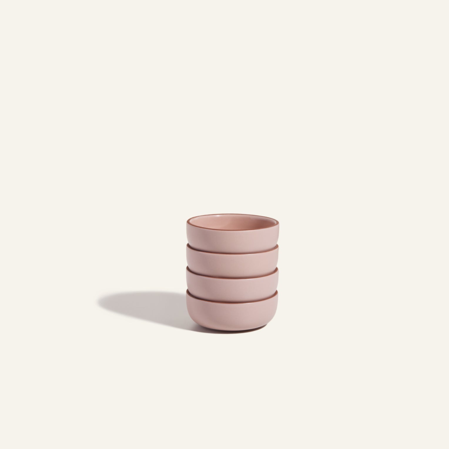 Four stacked Tiny Bowls, made from scratch-resistant ceramic in light pink, are arranged on a plain off-white background with a soft shadow cast to the left.
