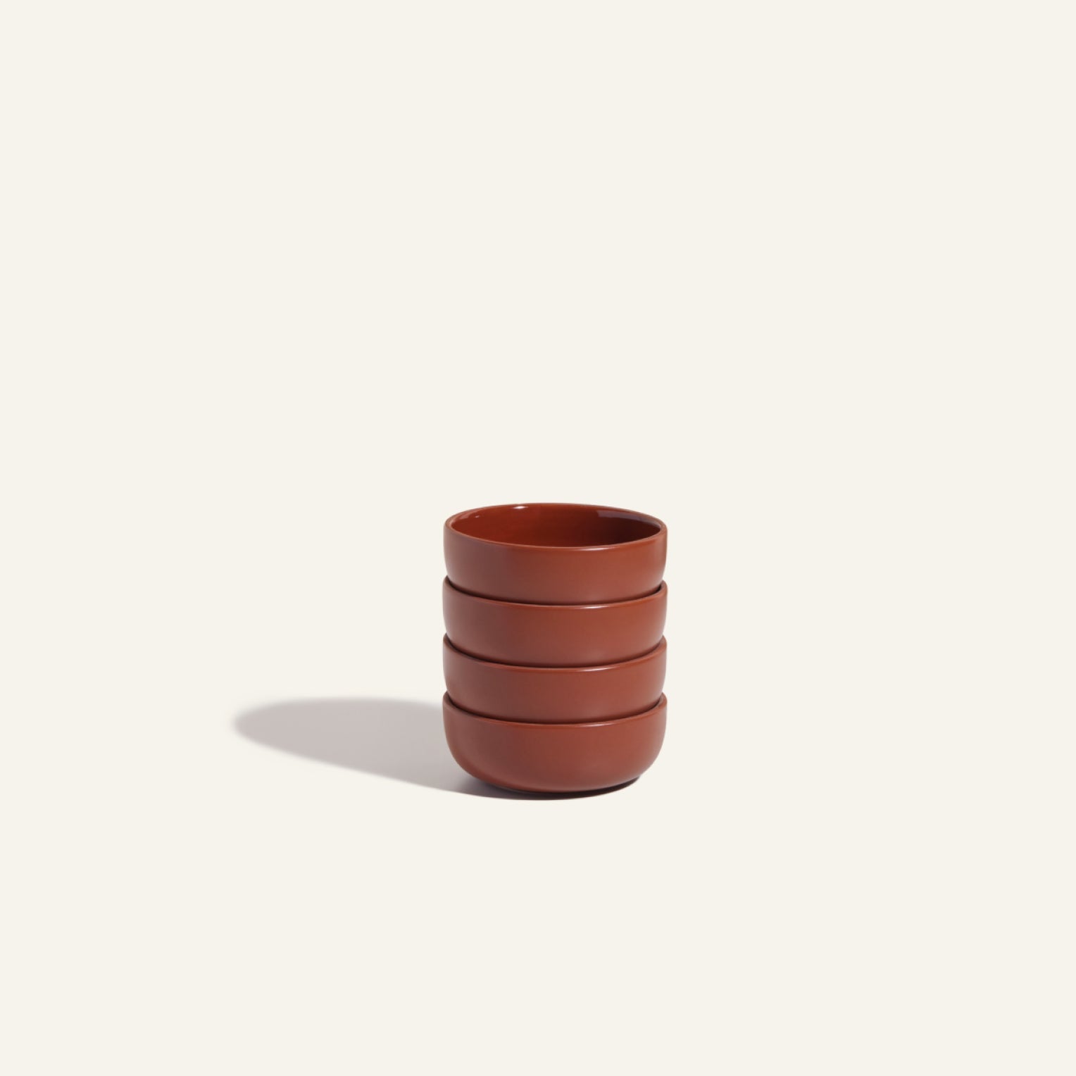 Tiny Bowls are four stackable ceramic bowls with a reddish-brown finish, shown on an off-white background. Scratch resistant and stylish, they offer durable tableware ideal for everyday use.