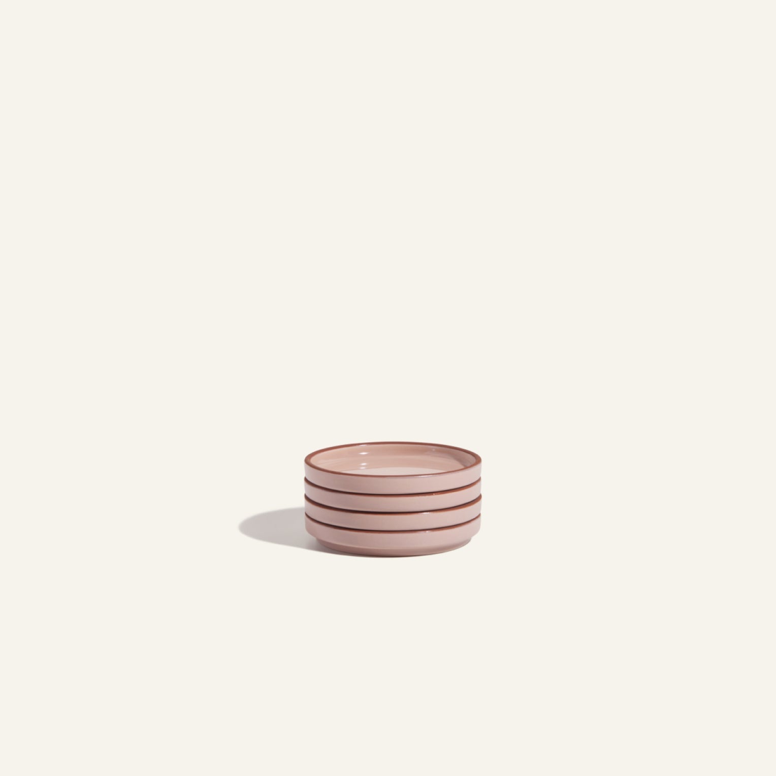 The Tiny Plates ceramic snack plate, small and light pink with three dark horizontal stripes, rests on a plain off-white background, casting a soft shadow.