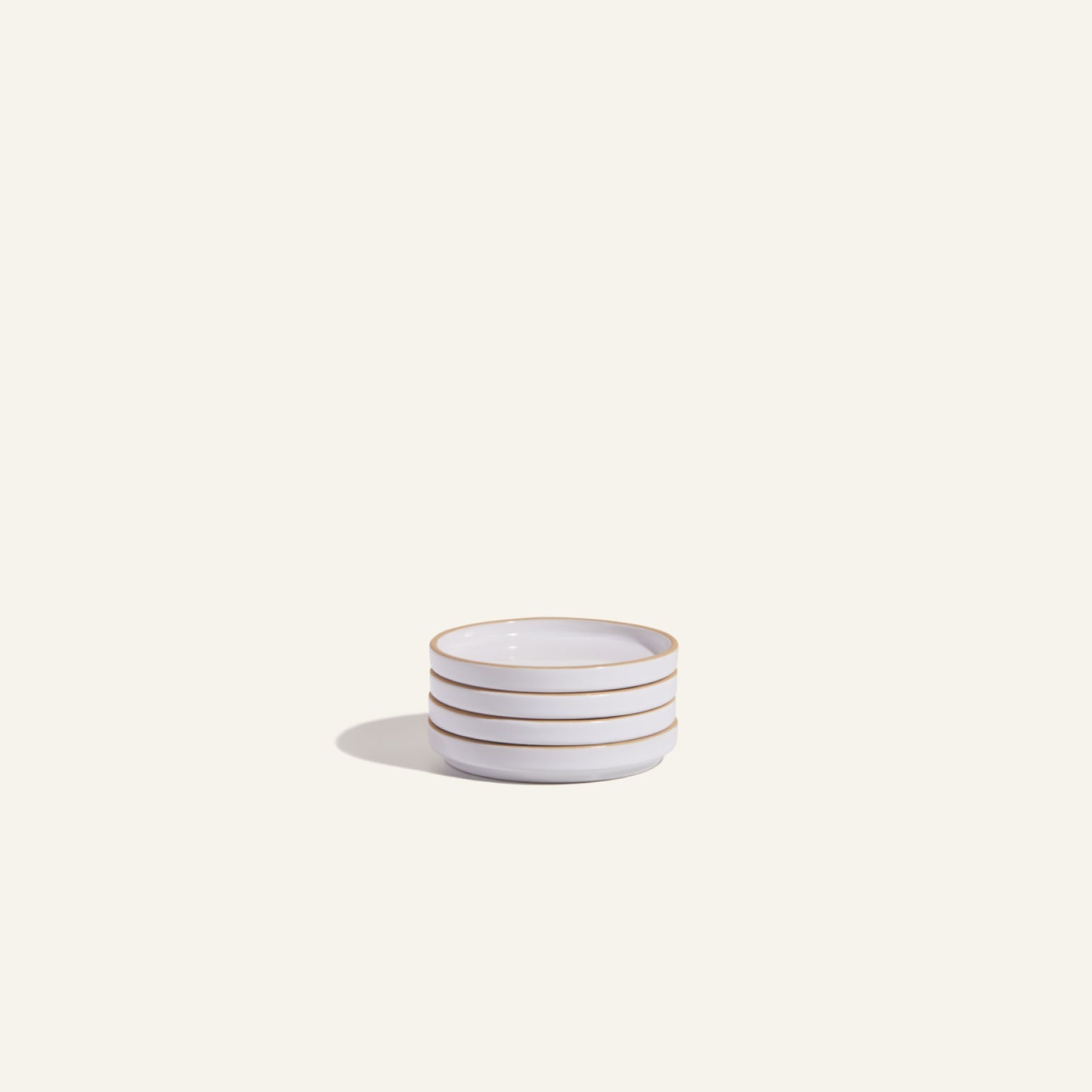 A Tiny Plates small white ceramic bowl with three horizontal brown stripes sits on a light surface, casting a faint shadow to the left.