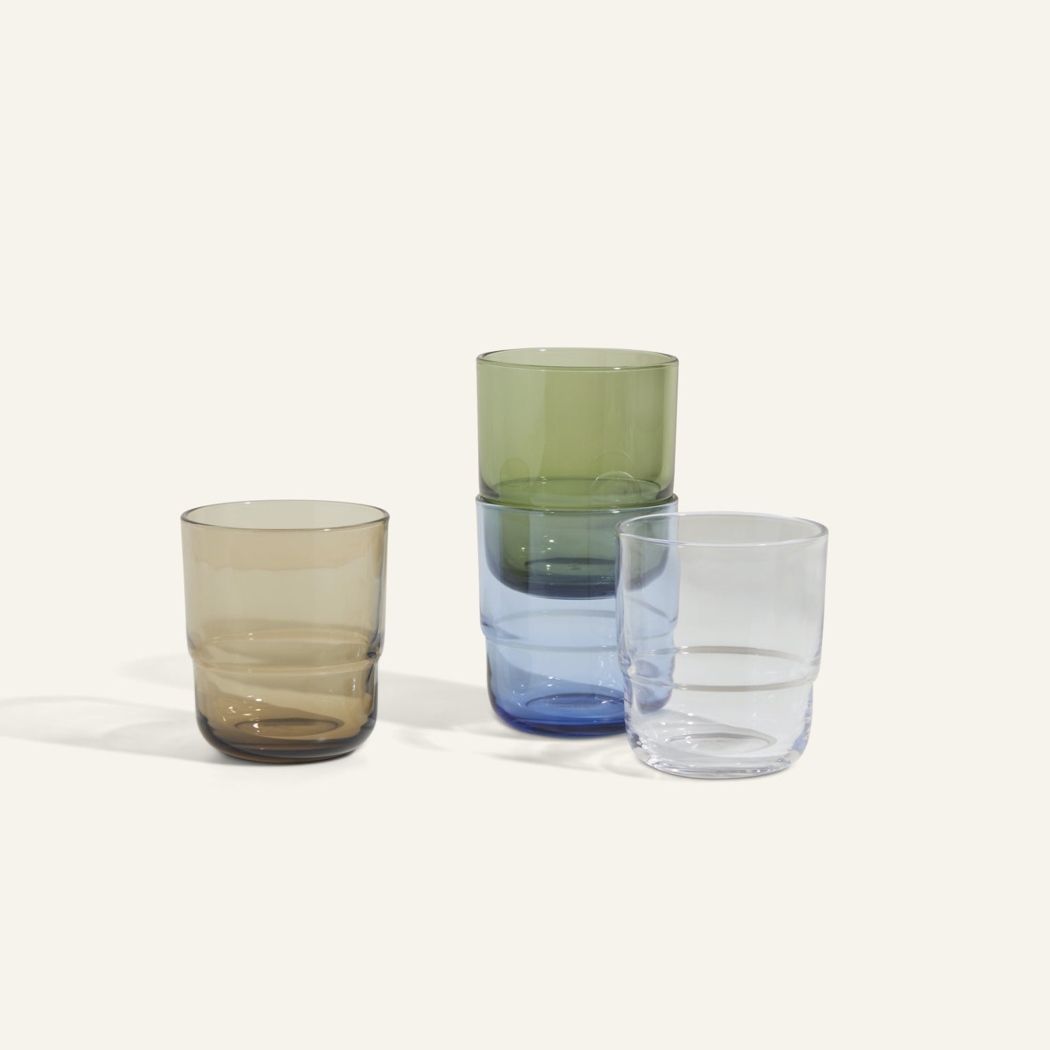 Four Short Night + Day Glasses are arranged on a light surface: two stacked, handmade tumblers in green and blue, and two recycled glass tumblers in brown and clear.