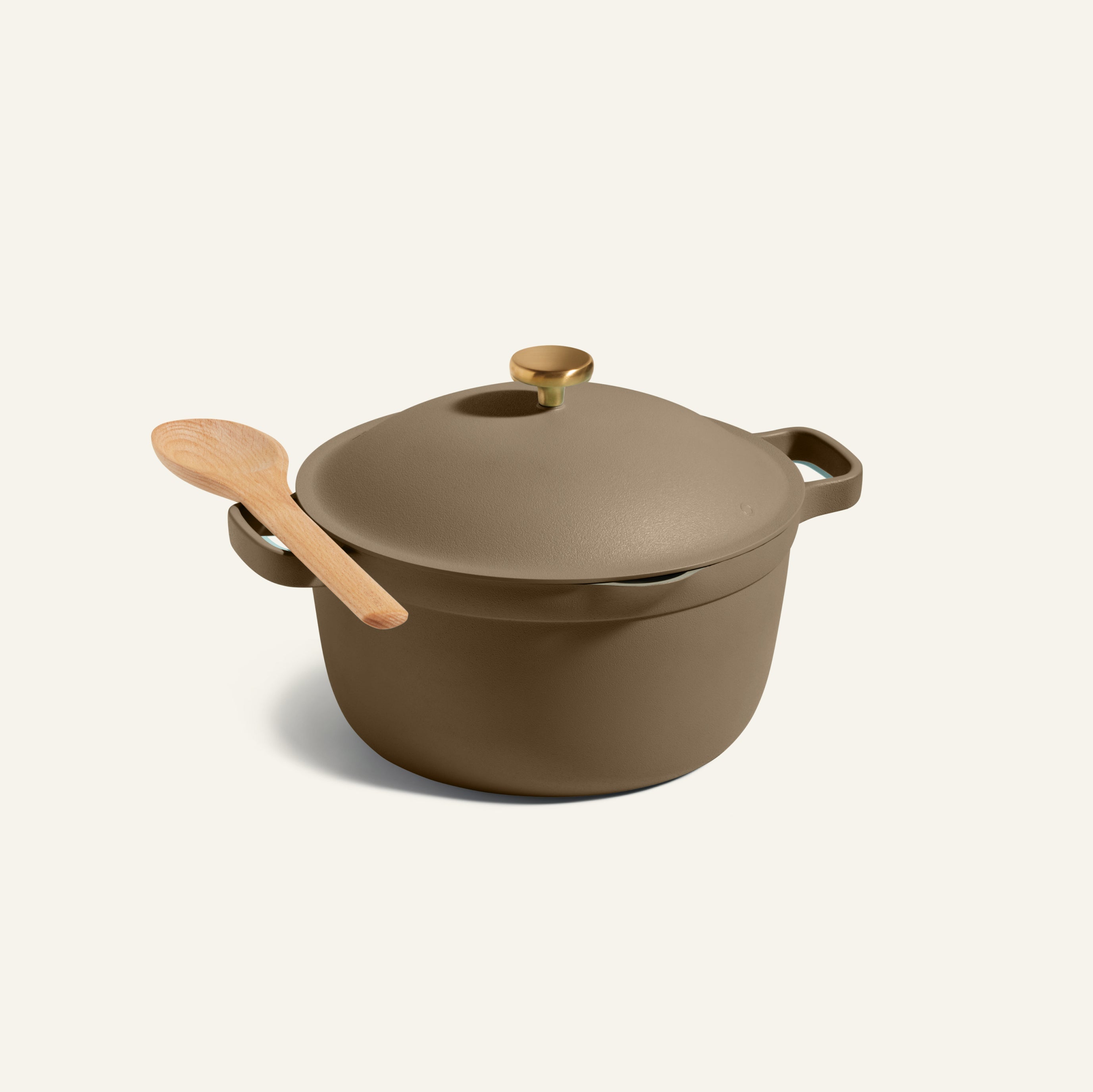 The Perfect Pot, a brown family-sized pot with two handles, a gold knob, and a wooden spoon resting on top, is pictured against a plain light background.