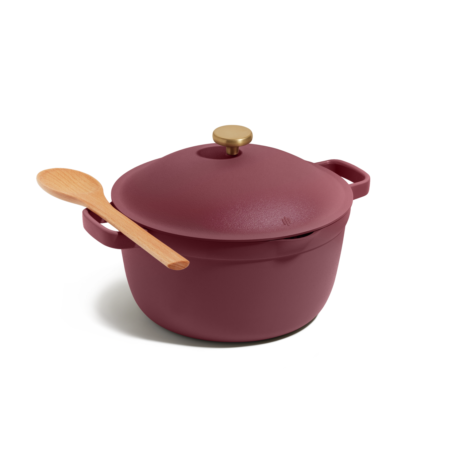 The Perfect Pot, a maroon cast iron Dutch oven with a gold knob, is displayed on a white background with a wooden spoon resting on its lid. This versatile pot is ideal for family meals.