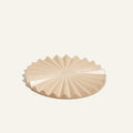 The Pleat Trivet is a beige ceramic plate with a geometric starburst pattern and ridged, angular edges—ideal as a decorative kitchen accessory or unique sunburst trivet, shown on a plain light background.