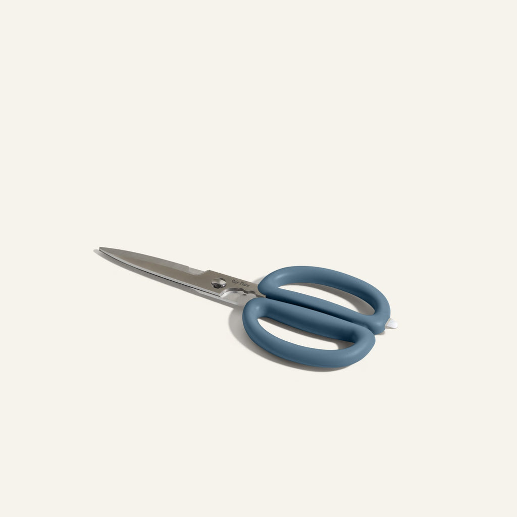 The Shear Genius stainless steel kitchen shears feature blue ergonomic handles and a multifunctional design with built-in herb strippers, shown on a plain light background.