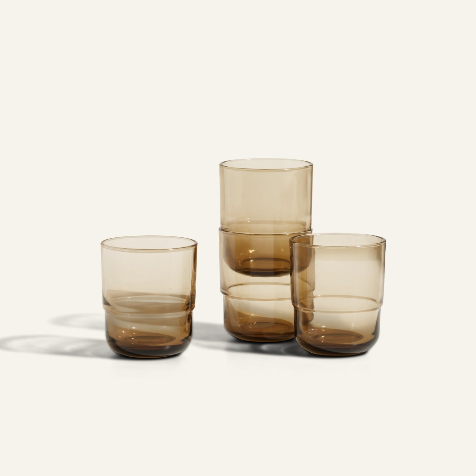 Four Short Night + Day Glasses, made from translucent brown recycled glass, are arranged in two stacks against a plain light background.