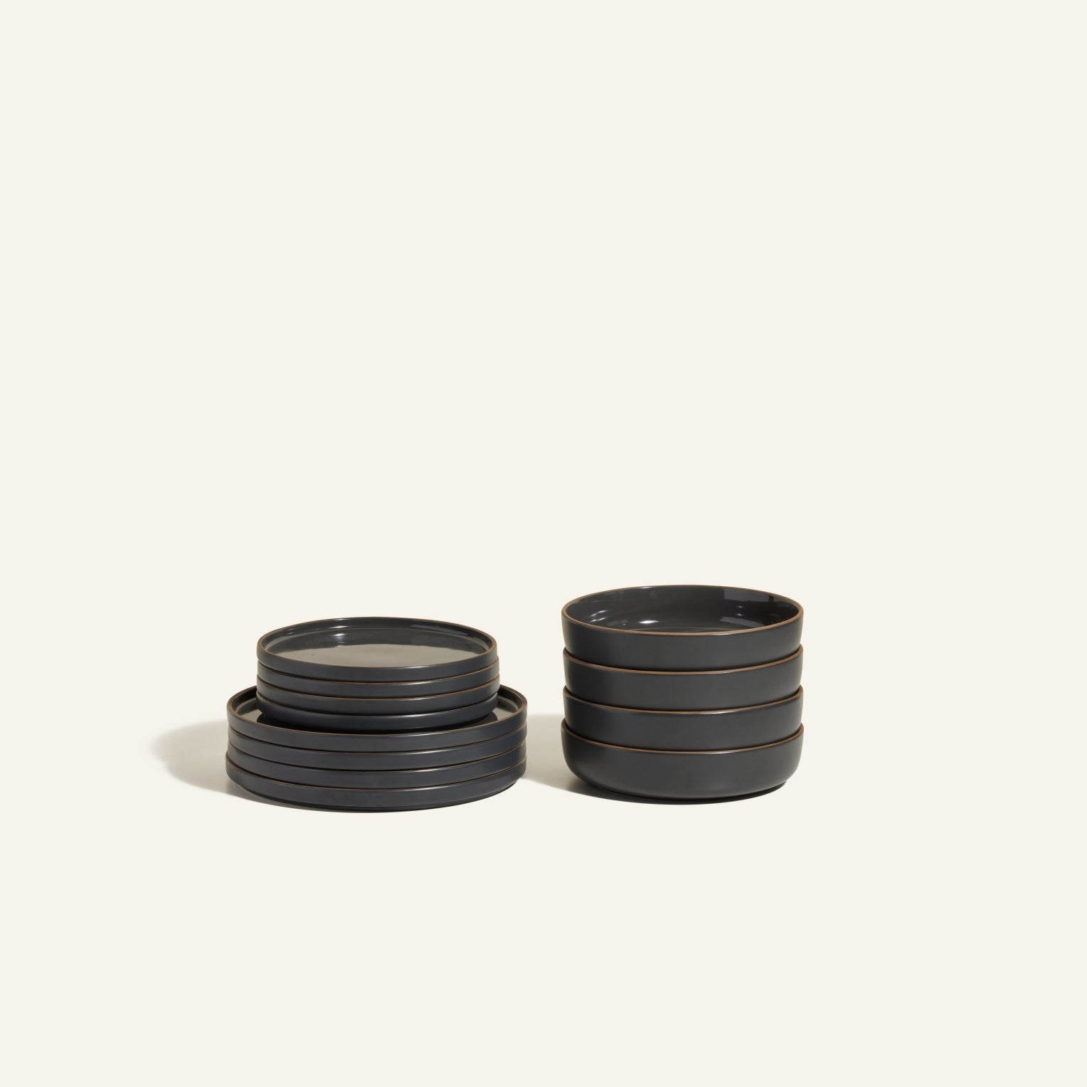 The Starter Stacking Set features two stacks of dark gray, hand-glazed ceramic tableware—one stack of flat plates and one stack of shallow bowls—ideal for kitchen owners seeking elegant essentials.