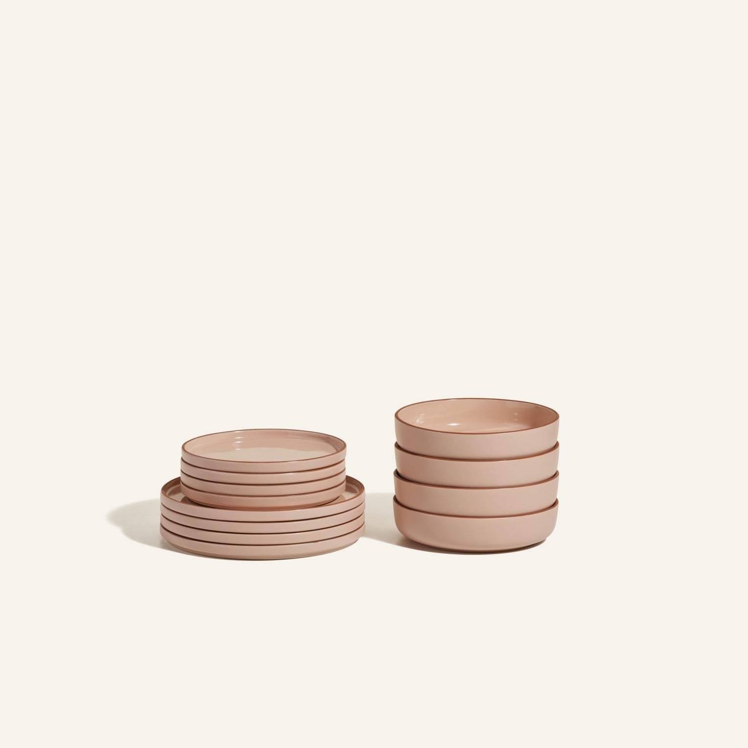 The Starter Stacking Set features eight hand-glazed light pink plates stacked on the left and four matching bowls on the right, offering elegant tableware for any kitchen, all set against a plain off-white background.
