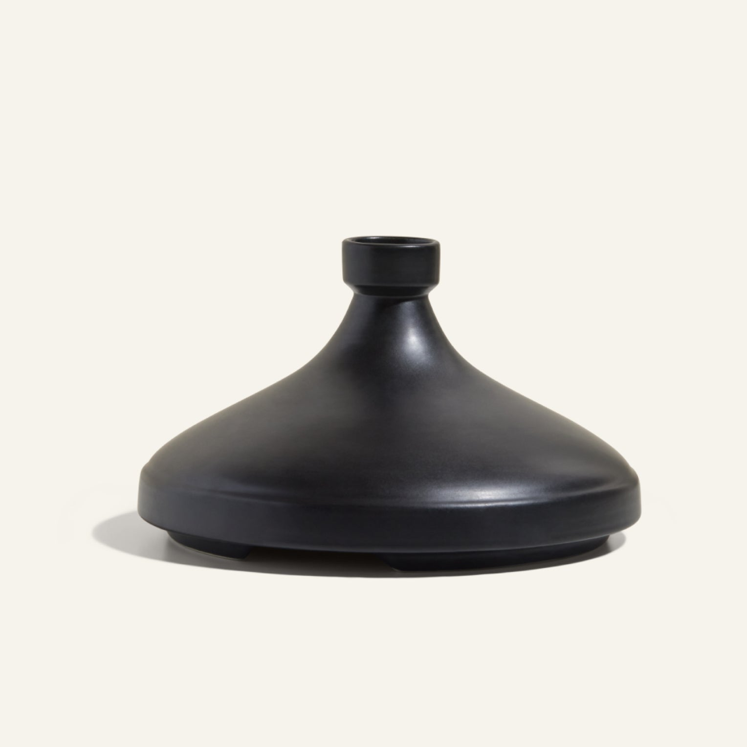 The Tagine is a matte black, dome-shaped ceramic vessel with a narrow neck and small opening, inspired by handcrafted Moroccan clay tagines and displayed against a plain light background.
