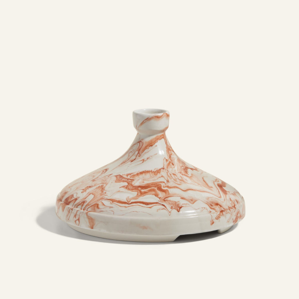 The Tagine is a handcrafted round Moroccan clay lid with a small handle, featuring a white base and brown marble-swirl pattern—ideal for slow cooking and traditional recipes.