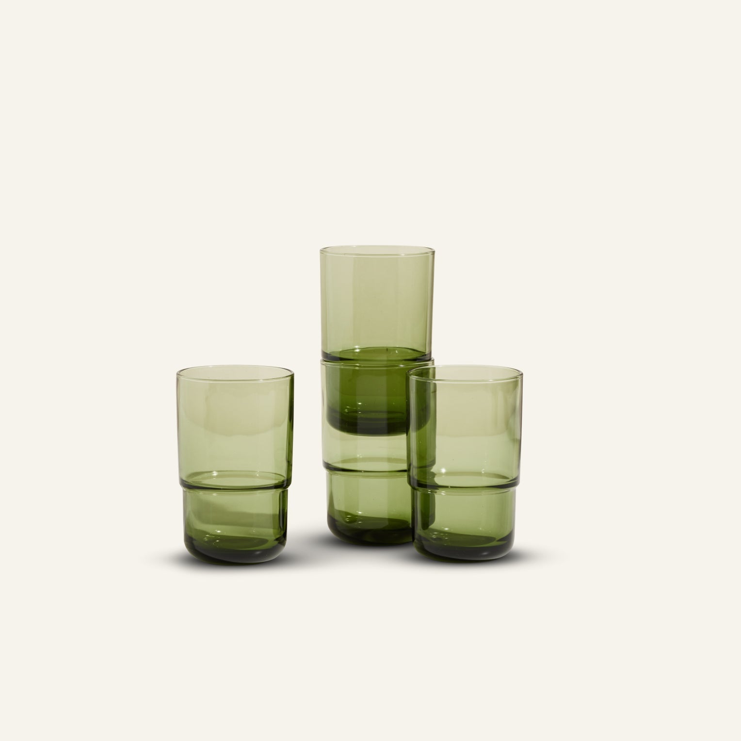 Three Tall Night + Day Glasses in green, featuring a minimalist stackable design, are arranged in a staggered formation on a plain light background.