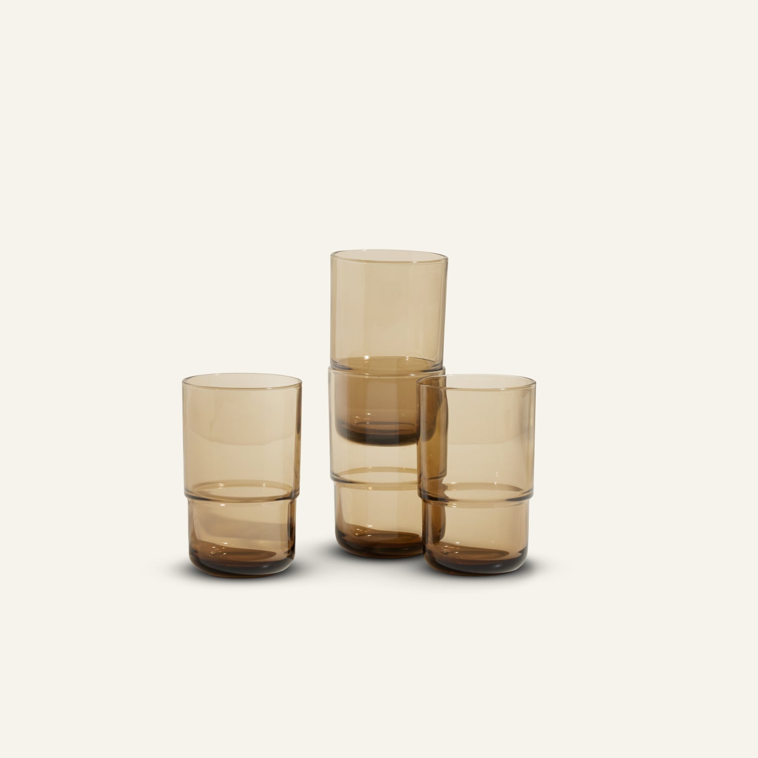 Four Tall Night + Day Glasses in amber are arranged with two stacked and two standing individually against a plain, light background.