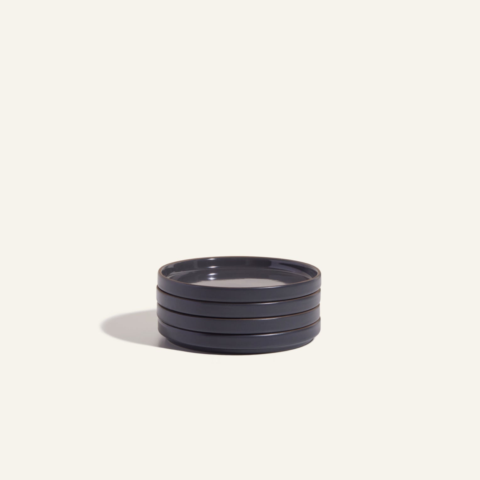 A stack of four round, dark-colored Dessert Plates made from scratch-resistant ceramic sits on a plain light background, casting a shadow to the left.