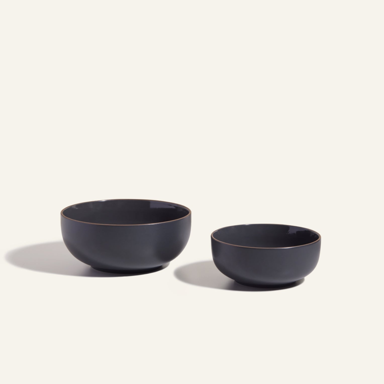 Two black Serving Bowls of different sizes sit on a light surface, casting shadows to the left.