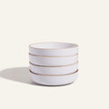 A set of four white scratch-resistant Dinner Bowls with a thin gold rim, stacked together on a plain light background.