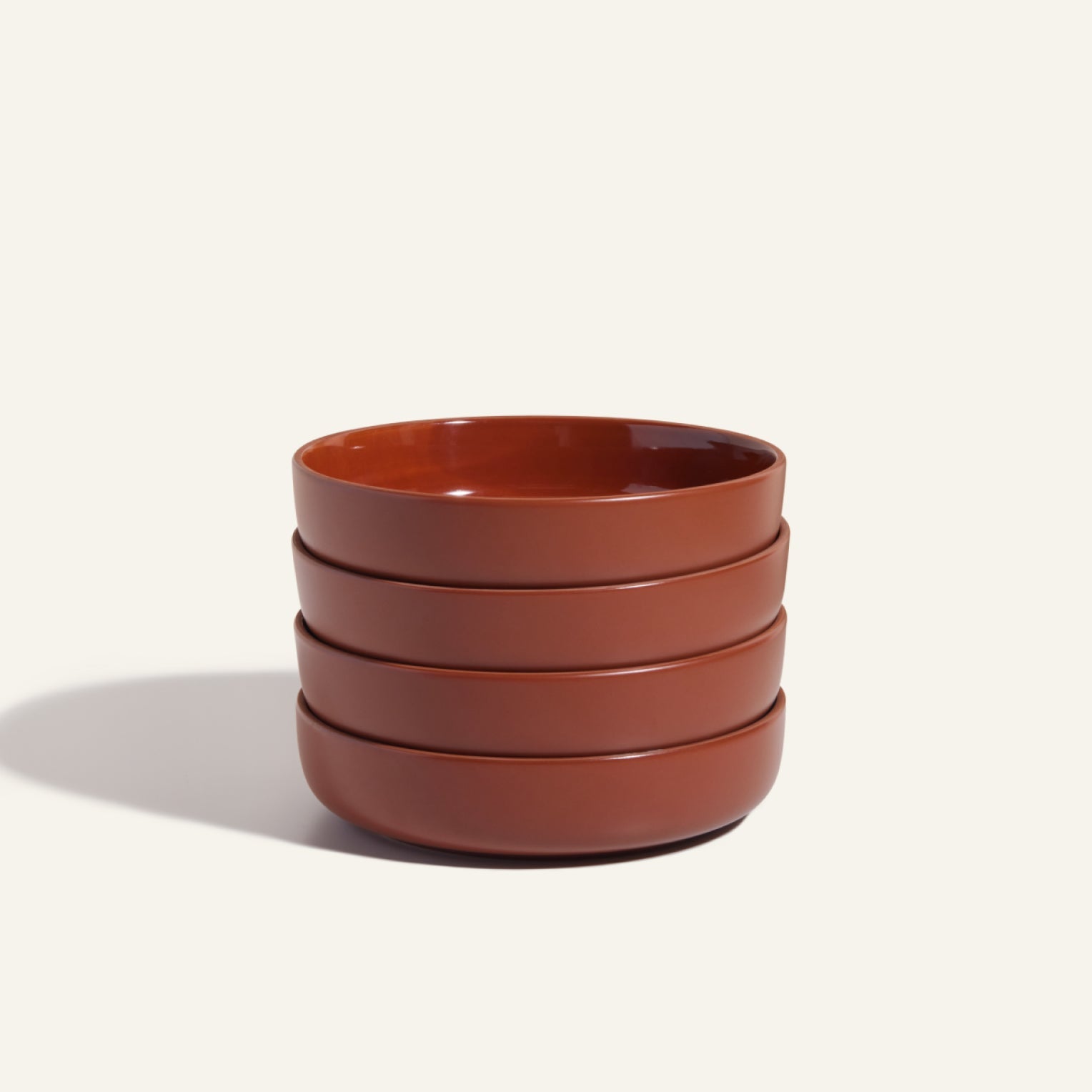 Four stackable, round brown Dinner Bowls are displayed against a simple off-white background, showcasing their versatile ceramic tableware design.