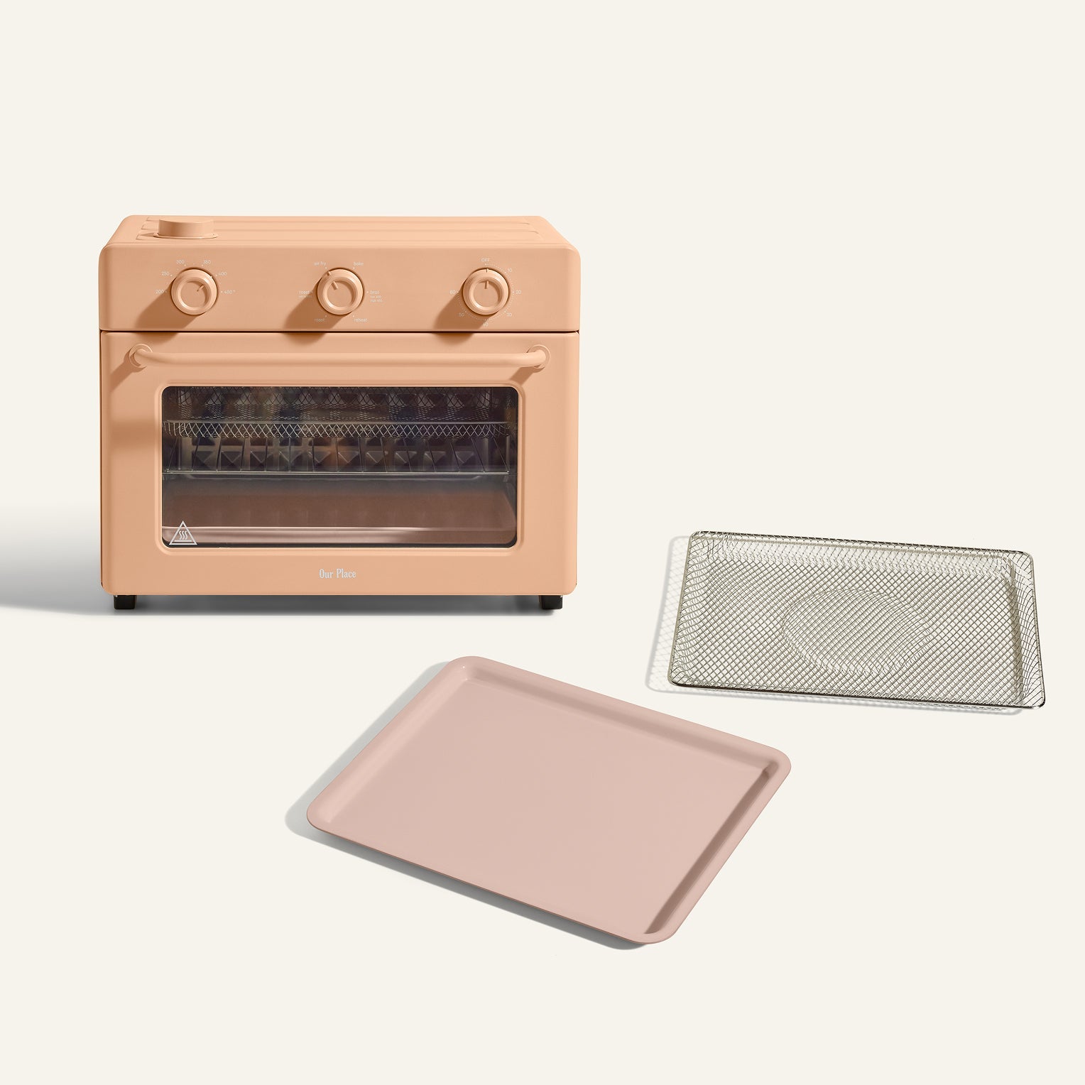 The Large Wonder Oven + Essentials Kit in beige features three dials and is displayed with a metal mesh tray and solid baking pan placed in front of it on a neutral background.