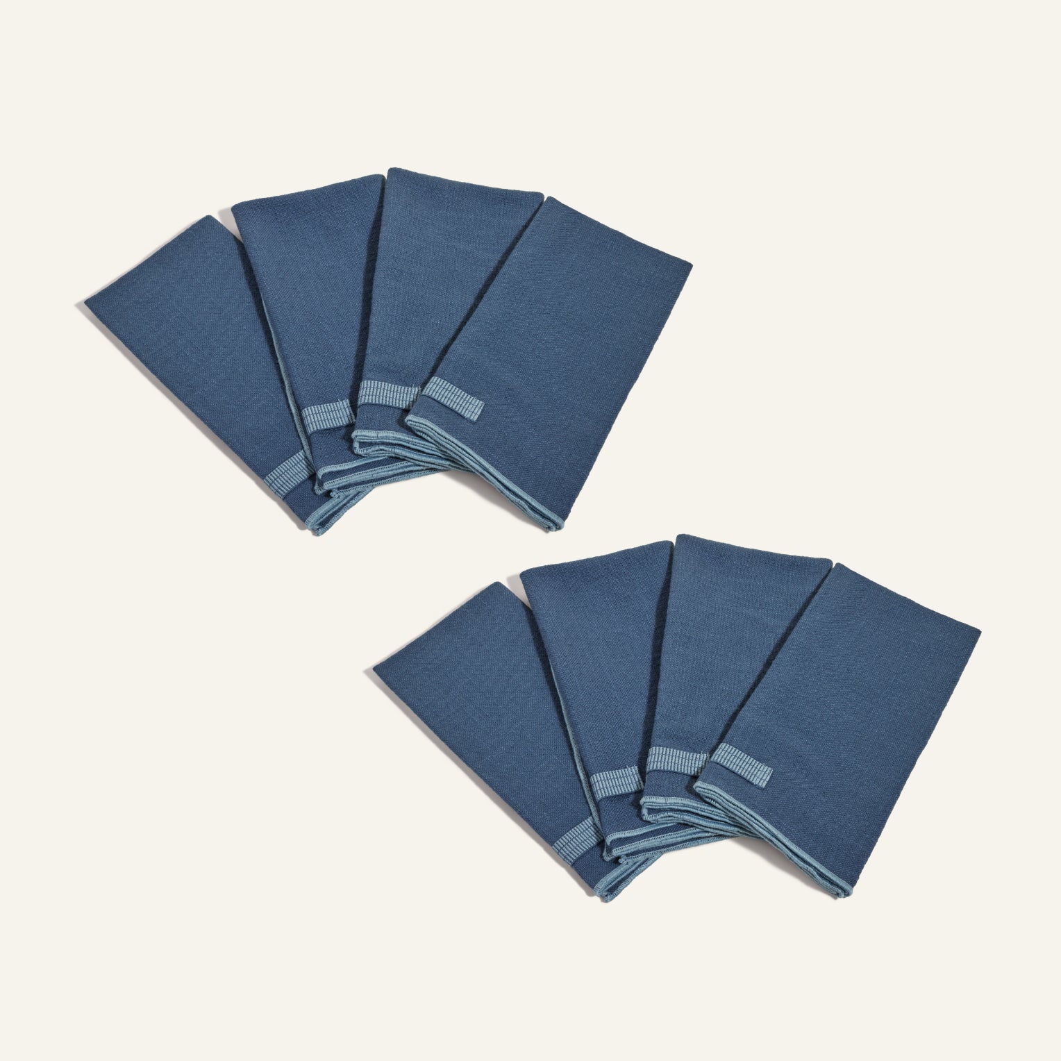 Eight blue Loop Napkins, each with a built-in loop ring, are arranged in two groups on a plain light background.