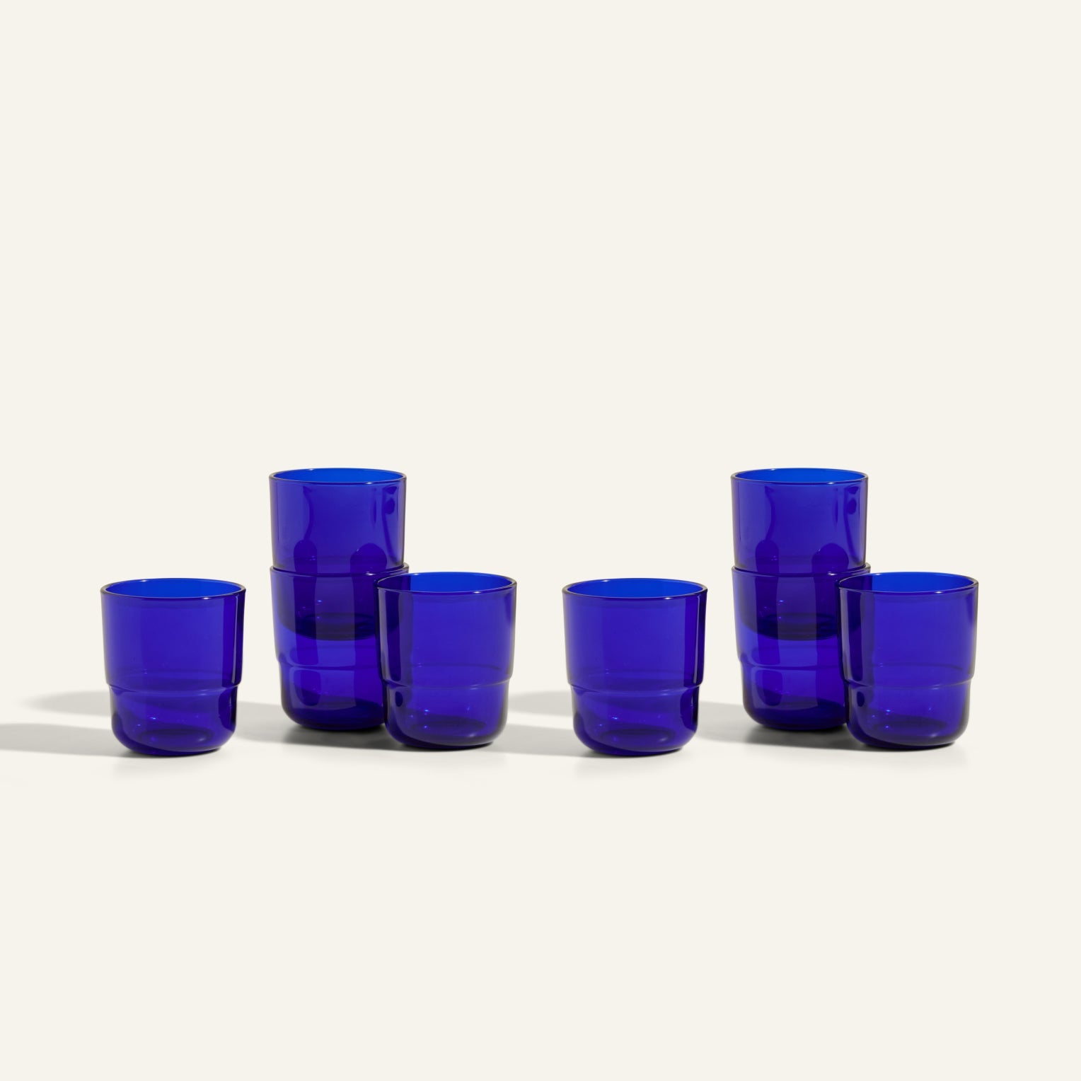Six Short Night + Day Glasses made from cobalt blue recycled glass are arranged in two rows on an off-white background—three are stacked in pairs and three stand alone, highlighting their handmade, versatile drinkware design.