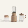 The Splendor Blender + Splendor Blender Everything Kit features a beige blender, two interchangeable clear containers, and a clear lidded mug, all showcased against a simple light background.