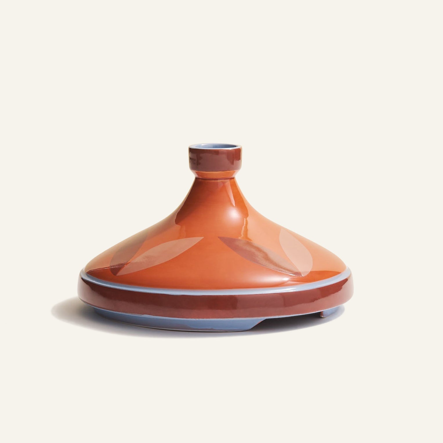 The Tagine is a handcrafted Moroccan clay dish with a conical lid and geometric leaf patterns, set on an off-white background—ideal for slow-cooking traditional meals.