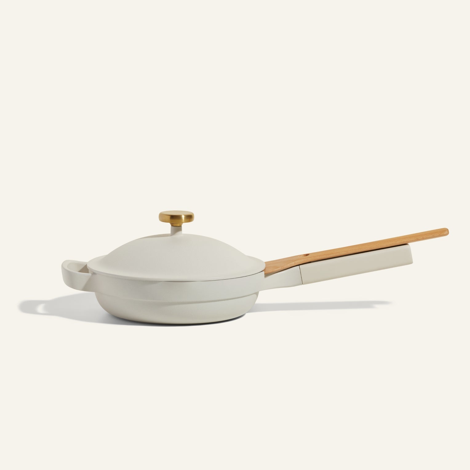 The Mini Always Pan 2.0, a beige nonstick pan with a matching lid, long wooden handle, and gold-colored knob, is shown on a plain light background—offering multifunctional style and convenience for any kitchen.