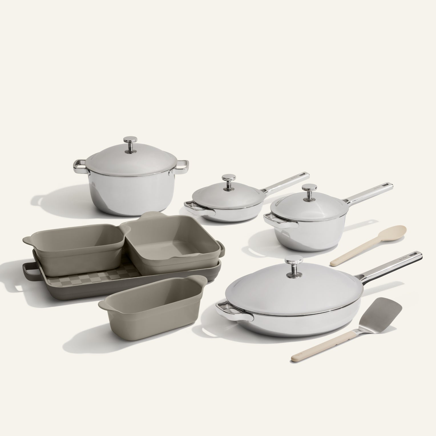 The VIP Titanium Pro Complete Cookware + Bakeware Set, featuring titanium pots, pans, lids, beige nonstick bakeware dishes, a wooden spoon, and spatula, is arranged on a plain light background.