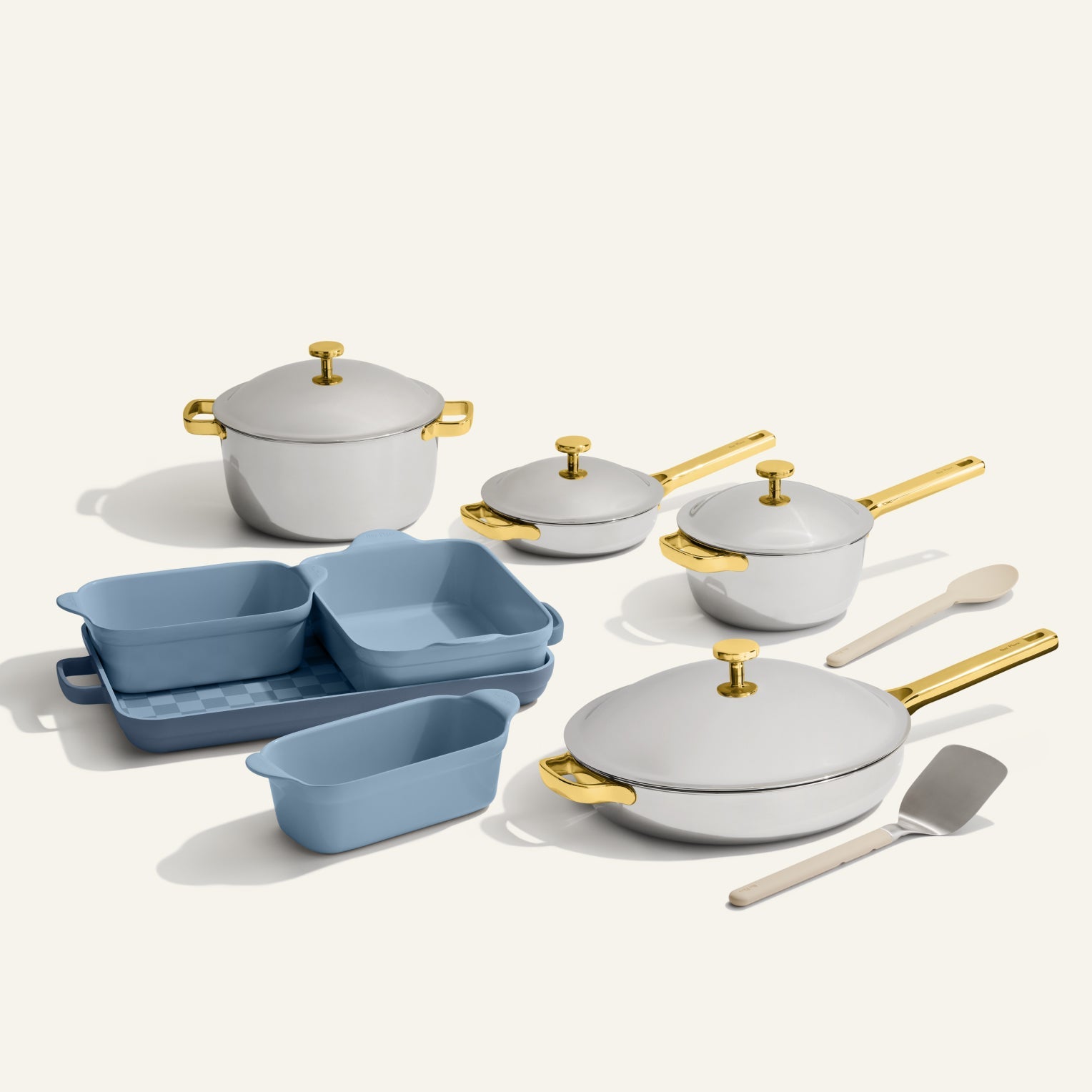 The VIP Titanium Pro Complete Cookware + Bakeware Set includes white pots and pans with gold handles, three blue nonstick bakeware dishes, a spatula, and a wooden spoon—all stylishly arranged on a light background.