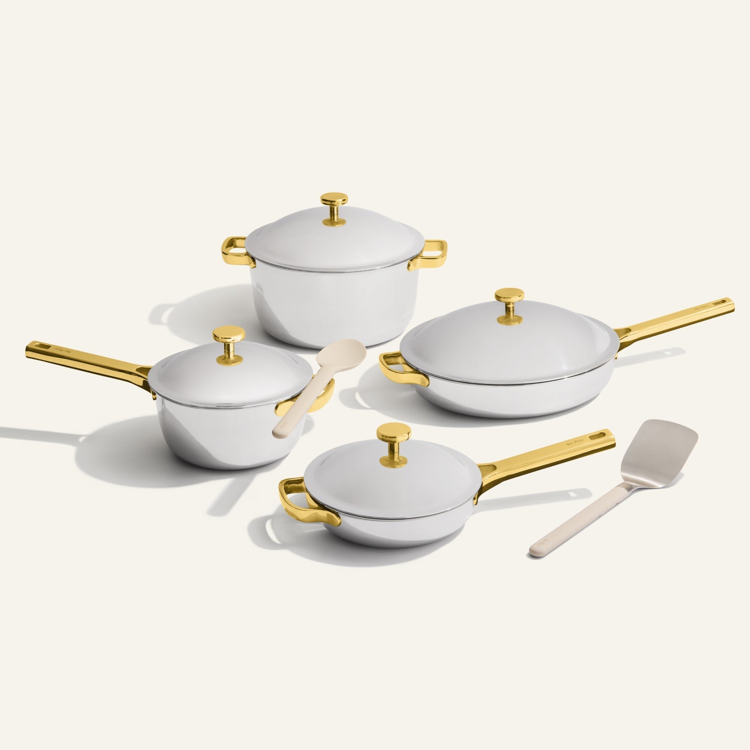 The VIP Titanium Pro Complete Cookware Set features four white pots and pans with gold handles and lids, displayed on a light surface, alongside a white spatula and a silver spatula.