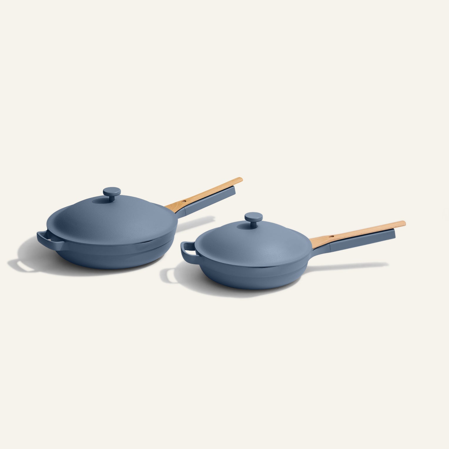 The Always Pan Duo includes two blue nonstick frying pans in different sizes, each with a wooden handle and matching lid, shown side by side on a light background.