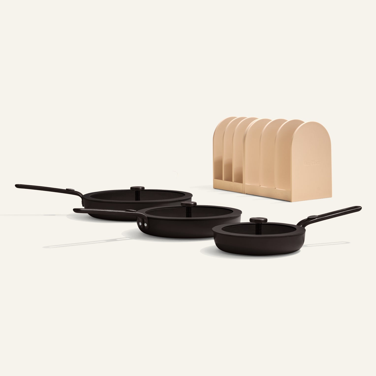 Set of black frying pans with a beige wooden block on a white background