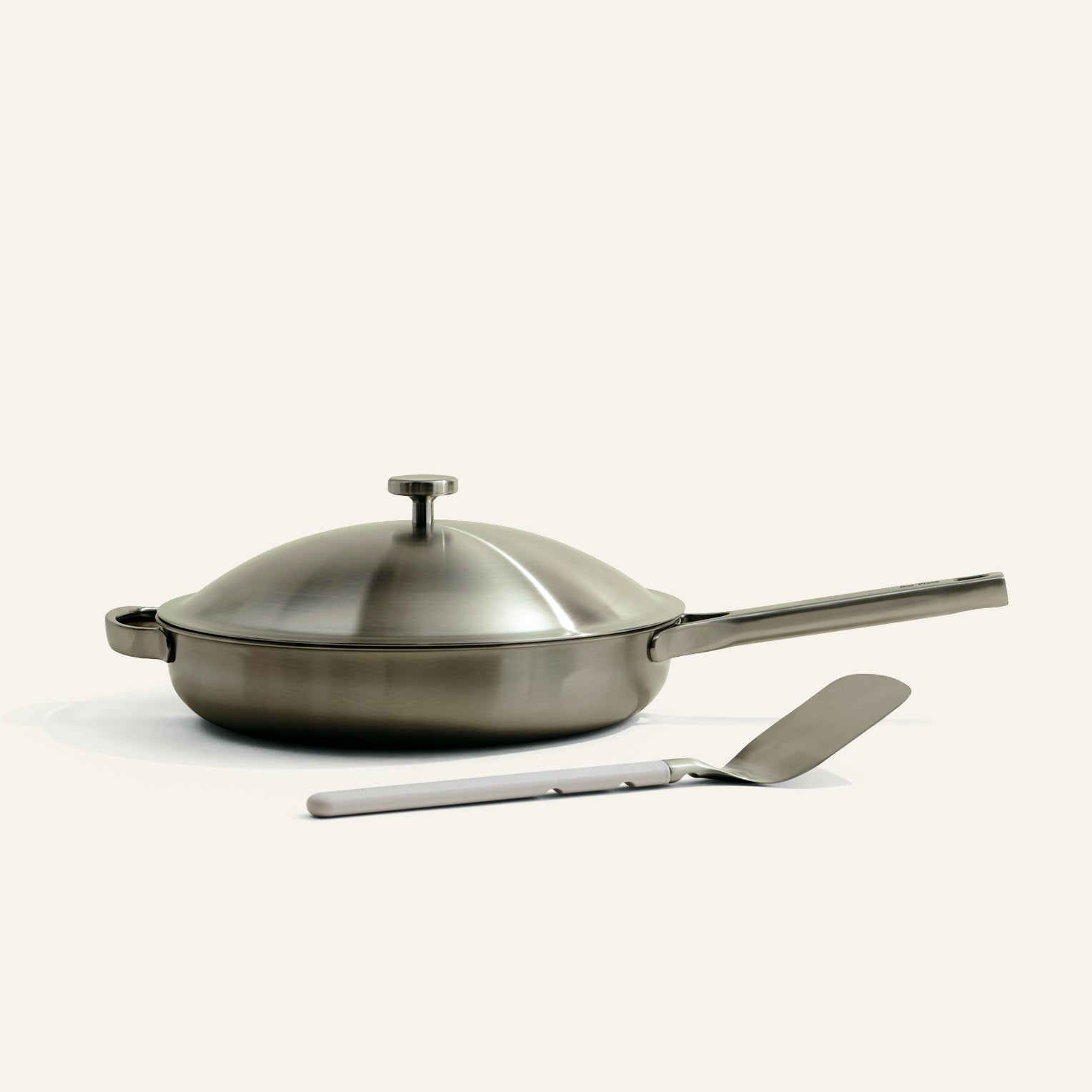 Stainless steel frying pan with lid and spatula on a white background