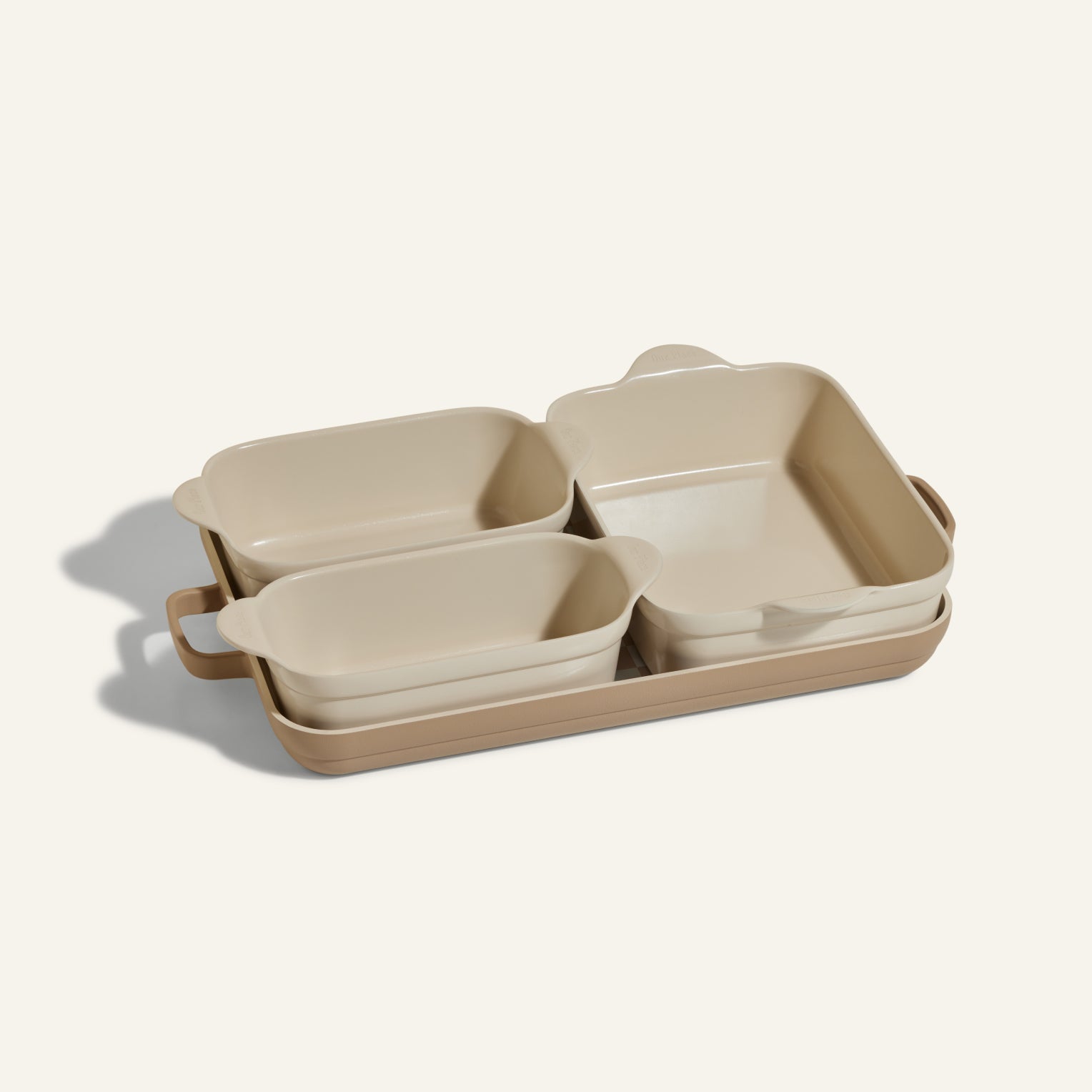 The Bakeware Set includes four beige ceramic baking dishes stacked on a large rectangular tray, making it an essential and versatile addition to any kitchen.