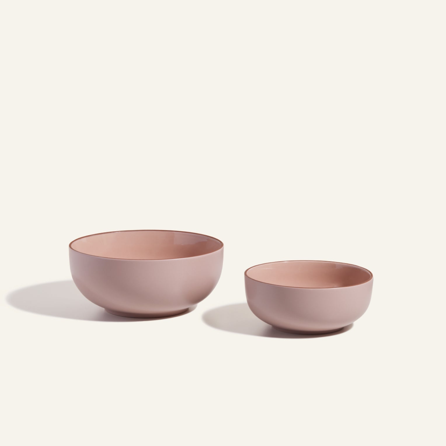 Two matte pink Serving Bowls of different sizes are displayed side by side on a plain background—ideal as stackable tableware for stylish salad presentations.