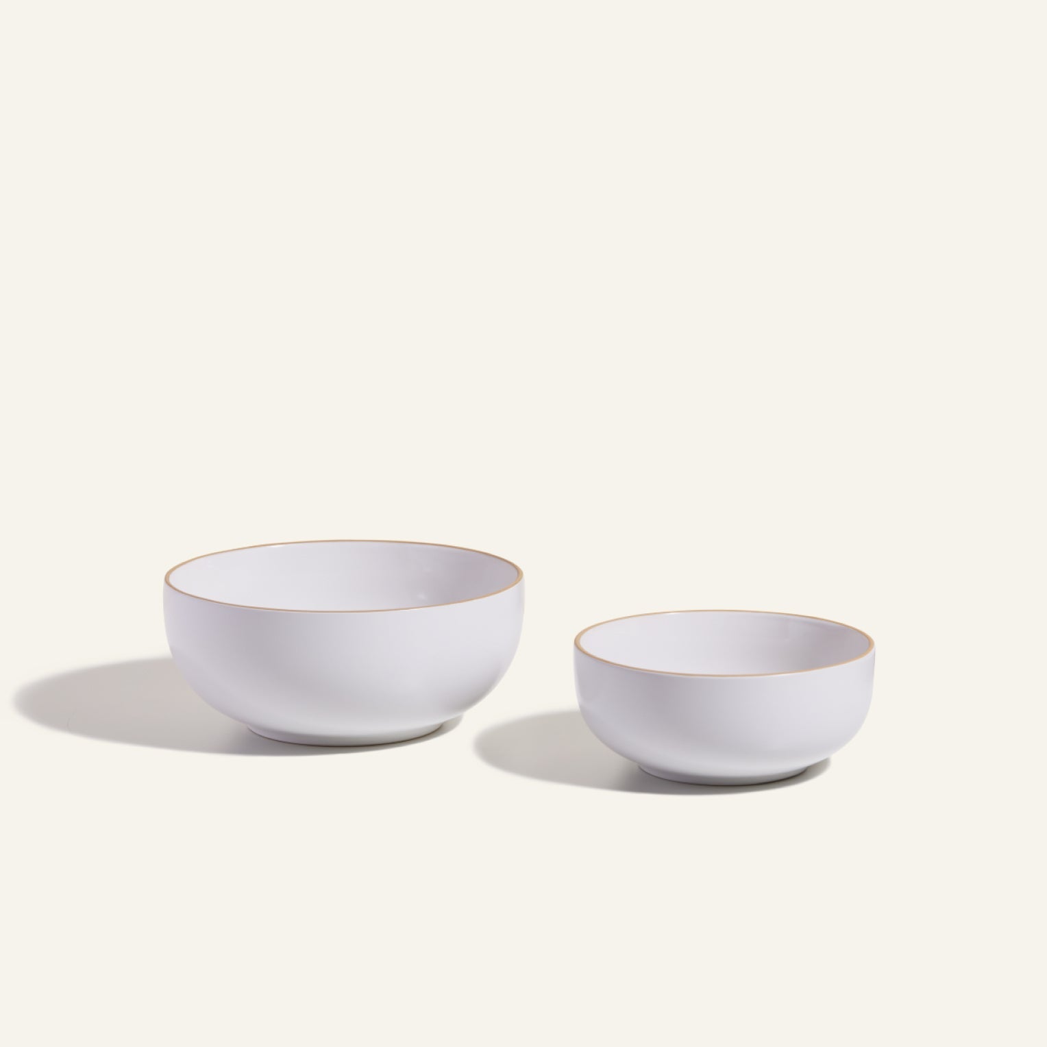 Two white Serving Bowls, featuring subtle gold rims in large and small sizes, are displayed side by side on a light background—ideal as elegant, stackable tableware for your next meal.